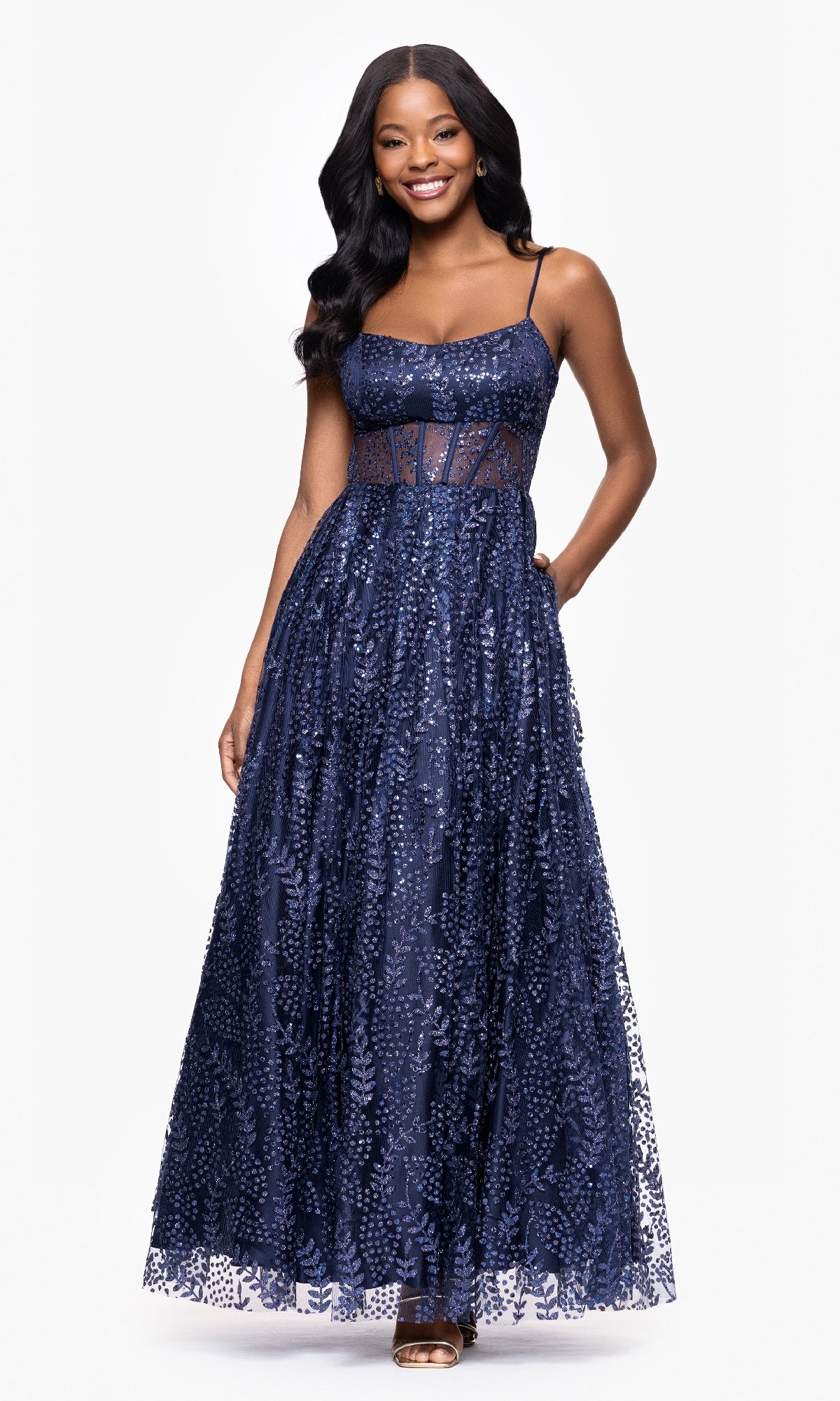 A woman in the Glitter-Print Prom Ball Gown: Blondie Nites 5539BN, featuring a navy blue, floor-length silhouette with a sheer corset bodice and lace details, smiles against a white background.